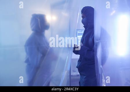 Blue tone portrait of two scientists or medical workers wearing full protective suits in biohazard danger zone Stock Photo