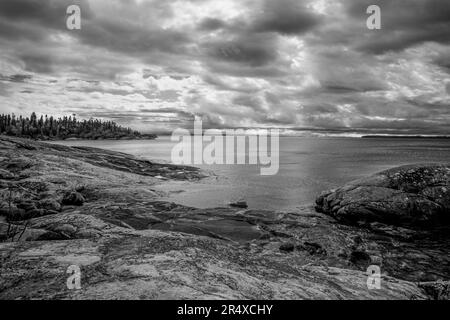 Dramatic clouds over Lake Superior and a rocky shoreline in infrared; Thunder Bay, Ontario, Canada Stock Photo