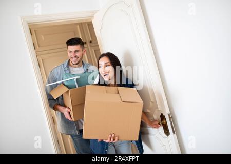 Real Estate. Happy Young Couple Entering New Home And Carrying Cardboard Boxes Stock Photo