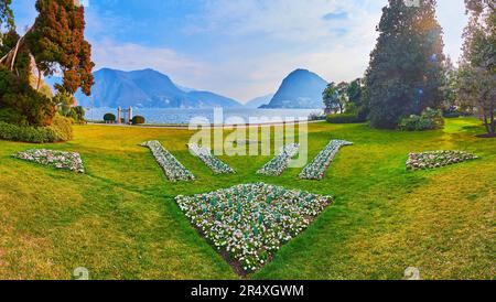 Green lawn, lush trees and ornamental flower beds in Ciani Park, located on the bank of Lake Lugano against the Monte San Salvatore, Lugano, Switzerla Stock Photo