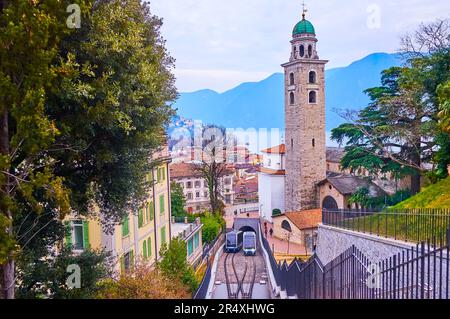 The modern wagons of Sassellina funicular (Citta-Stazione funicular), riding up and down in front of the tall bell tower of St Lawrence Cathedral, Lug Stock Photo