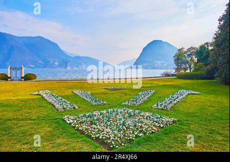 The green lawn and ornamental flower beds of daisies in Parco Ciani, located on Ceresio bank against the Monte San Salvatore, Lugano, Switzerland Stock Photo