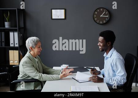 Side view portrait of smiling senior woman with disability speaking to HR recruiter in job interview Stock Photo