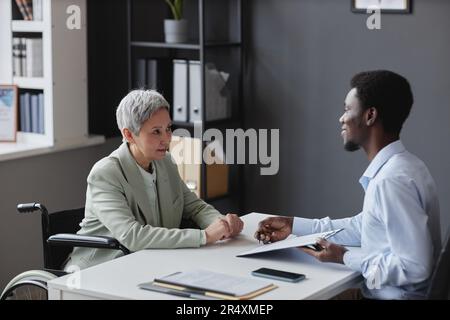Side view portrait of mature woman with disability speaking to recruiter in job interview Stock Photo