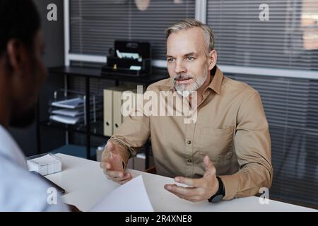 Portrait of bearded mature man speaking to recruiter during job interview Stock Photo