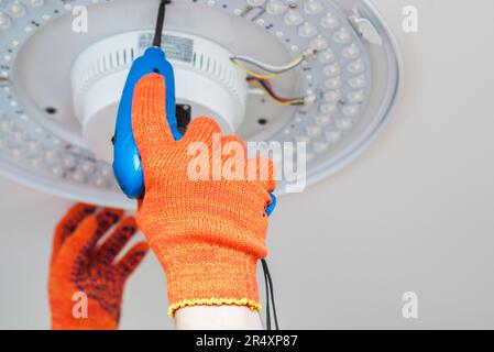 An electrician installs a chandelier on the ceiling. Stock Photo