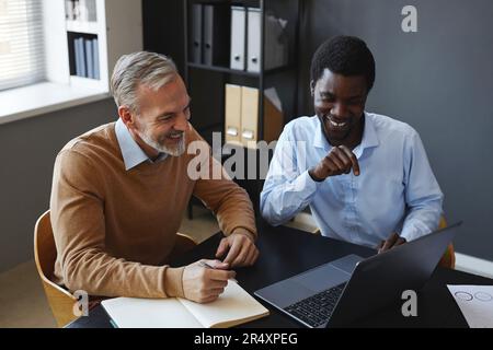 Portrait of black young businessman with senior colleague using laptop together at workplace in office Stock Photo