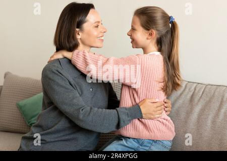 Cheerful pretty caucasian middle aged woman hugging small girl on sofa in living room Stock Photo