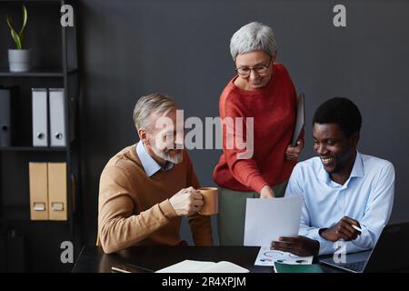 Group of three business people with senior workers collaborating on project together at workplace in office Stock Photo