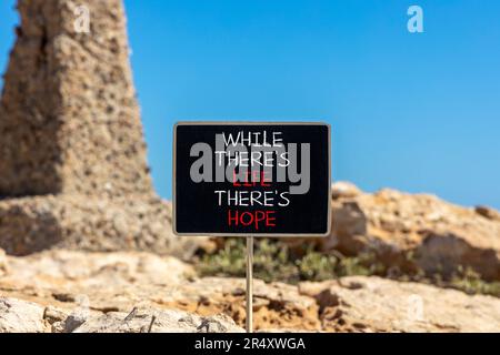 Life and hope symbol. Concept word While there is life there is hope on beautiful black chalkboard. Beautiful stone blue sky background. Business life Stock Photo