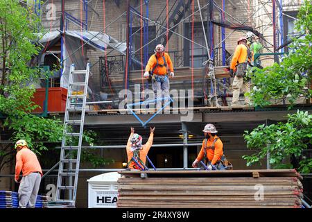 Scaffolders, construction workers dismantle scaffolding and a sidewalk shed surrounding a masonry brick building in Manhattan, New York City Stock Photo