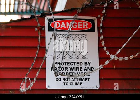 A 'Danger, Protected By Razor Wire And Barbed Wire, Do Not Attempt To Climb' signage surrounded by razor wire, on a storefront in New York City Stock Photo