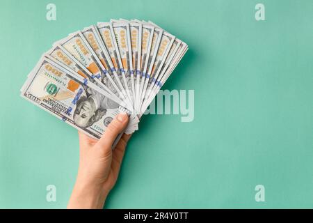A lot of bills of 100 dollars in hands are folded in a fan on a green background top view with space for text. Currency, banknotes in female hands. Stock Photo