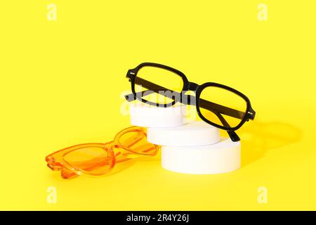 Podium with stylish sunglasses on yellow background Stock Photo