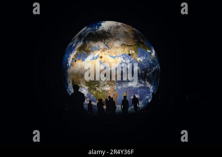 Brno, Czechia - July 12, 2020: People walking in front of inflatable Earth model illuminated at night, only their silhouettes visible Stock Photo