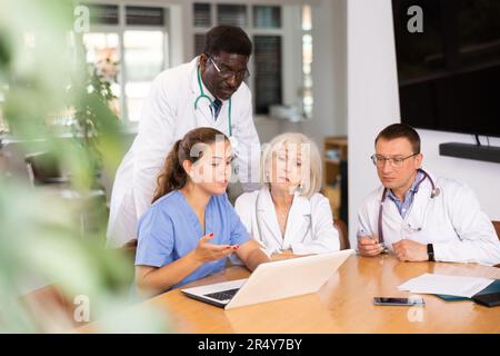 Doctors sitting around the table looking at the notebook Stock Photo