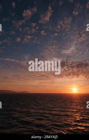Intense pinks and blues in evening sky with glowing cloudscape, ripples on ocean and distant islands Stock Photo