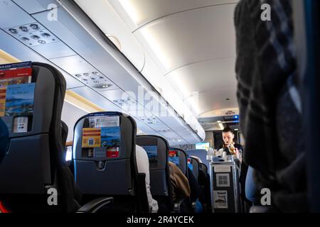 Flight attendant out of focus, blurred serving meal and drinks to passengers sitting in a chair in an airplane cabin Airbus A 320 Stock Photo
