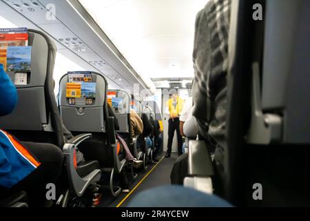 A flight attendant out of focus, blurred demonstrating life vest to passengers, low angle. Airbus A 320 Stock Photo