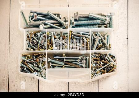 Silver and gold metal screws. Tool box with screws and bolts on a wooden white table. Stock Photo