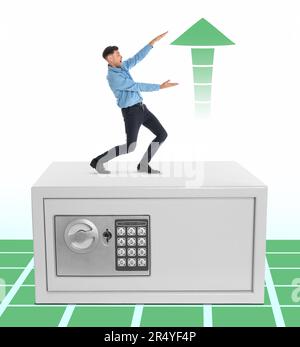 Multiplying wealth, increasing savings. Excited man pointing at green arrow up while standing on big steel safe against white background Stock Photo