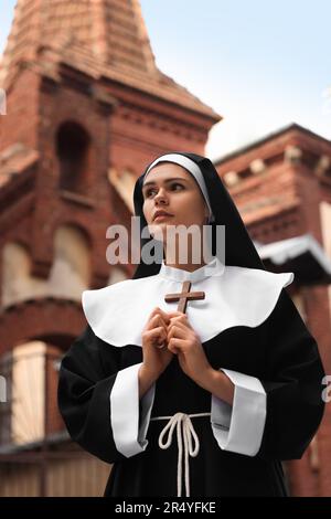 Young nun holding Christian cross near building outdoors Stock Photo