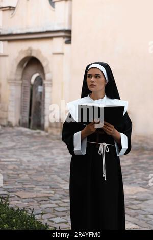 Young nun reading Bible on city street Stock Photo