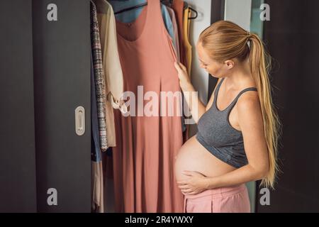 A pregnant woman has nothing to wear. A pregnant woman stands in front of a closet with clothes and does not know what to wear because the clothes do Stock Photo