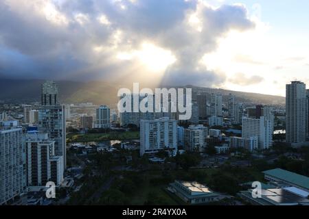 Shafts of golden light at sunrise pierce through the clouds, illuminating the buildings of downtown Honolulu. Stock Photo