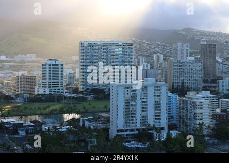 Shafts of golden light at sunrise pierce through the clouds, illuminating the buildings of downtown Honolulu. Stock Photo