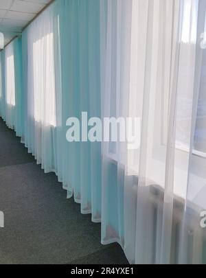 The prospect of a long hotel corridor with transparent curtains on large windows and blue tinting Stock Photo