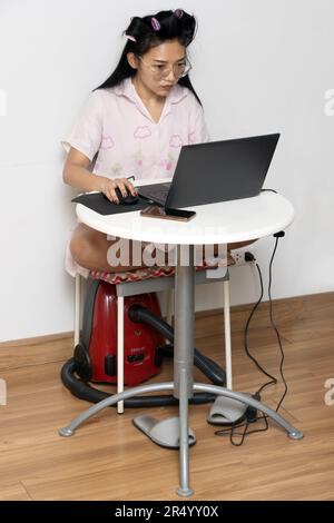 A young woman with curlers dressed in a nightgown is working on a laptop Stock Photo