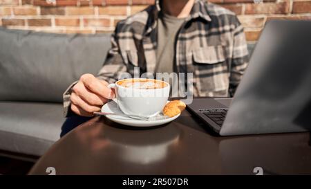 Handsome successful smart man looking at a laptop. A young man is sitting on the veranda in a cafe working and drinking coffee. Reading, browsing the Stock Photo