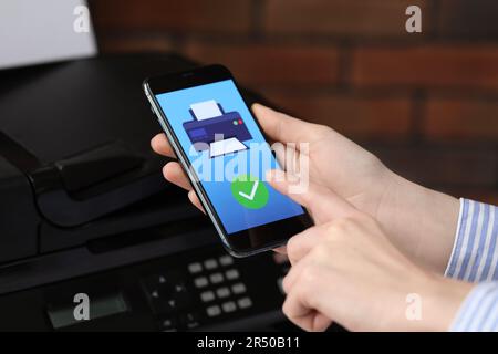 Man using printer management application on mobile phone indoors, closeup. Image on device screen. Stock Photo