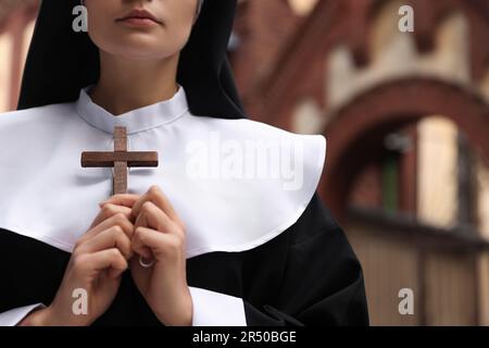 Young nun holding Christian cross near building outdoors, closeup Stock Photo