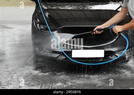 Man washing auto with high pressure water jet at car wash, closeup Stock Photo