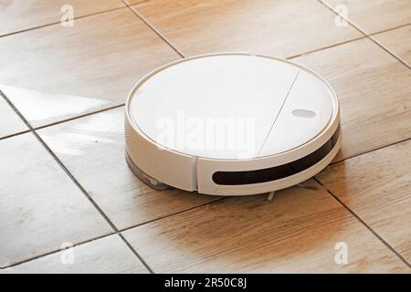 robot vacuum cleaner cleans and washes the floors on the tiled floor in the living room lit by the sun Stock Photo