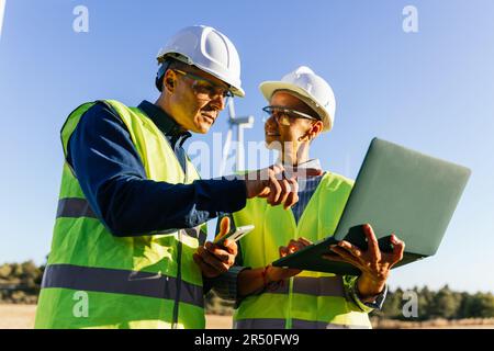 Engineers using a laptop while working together in the wind farm. Stock Photo