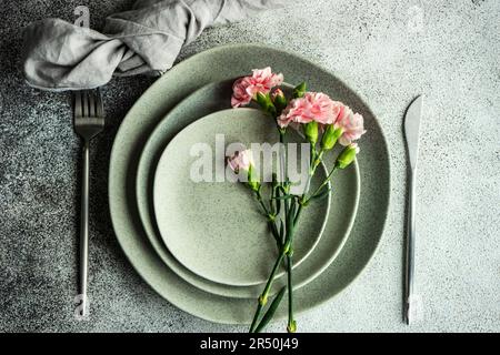 Minimalistic table setting in grey colors decorated with pink carnation flowers Stock Photo
