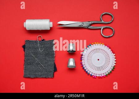 Flat lay composition with thimbles and different sewing tools on red background Stock Photo