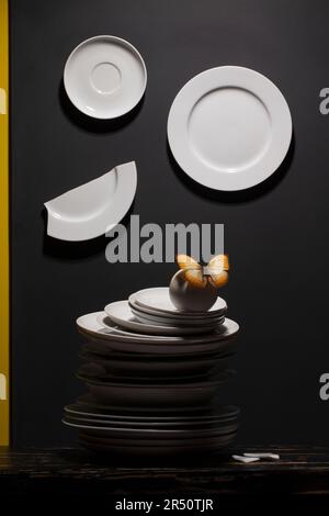 White plates and pile of plates with a butterfly on black background Stock Photo