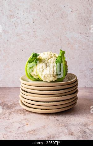 Organic cauliflower with leaves on a stack of fluted ceramic plates Stock Photo