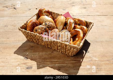 Various freshly baked goods in a basket on a wooden table (rolls and pretzels) Stock Photo