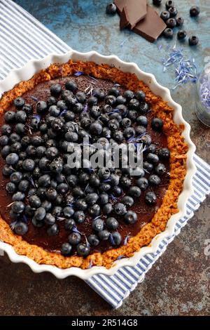 Tart with chocolate mass and blueberries, sprinkled with dried cornflower flakes and powdered sugar Stock Photo