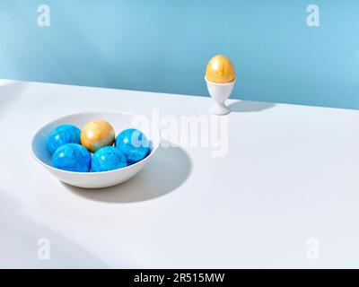 Blue and yellow Easter eggs in a bowl and in an egg cup Stock Photo