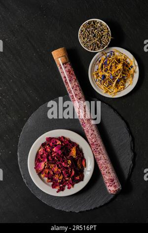 Rose blossoms, lavender blossoms and flower mix in small bowls and glass tube with flower salt on slate plate Stock Photo