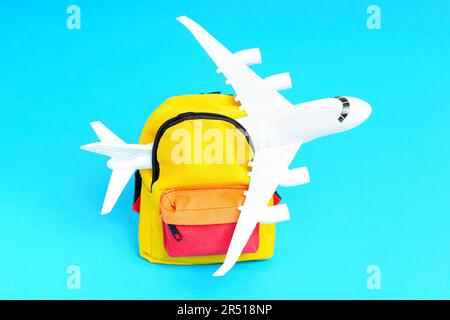 Miniature toy airplane sticking out of a small colorful backpack isolated on blue background. Vibrant travel and adventure related backdrop. Stock Photo