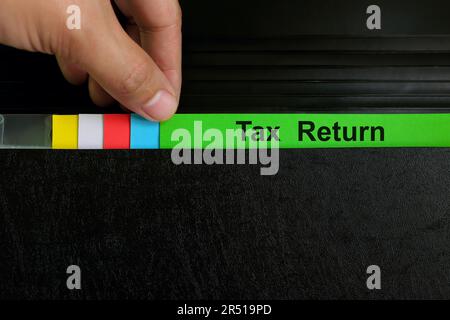 Hand picking tax return file record in black binder folder. Filing, accounting and taxation concept. Stock Photo