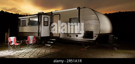 Brightly lit camping trailer at sunset with a dark ridge and bright clouds behind Stock Photo