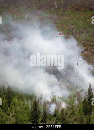 A helicopter carries a bucket of water over forest fire smoke in Kootenay National Park, British Columbia, Canada Stock Photo